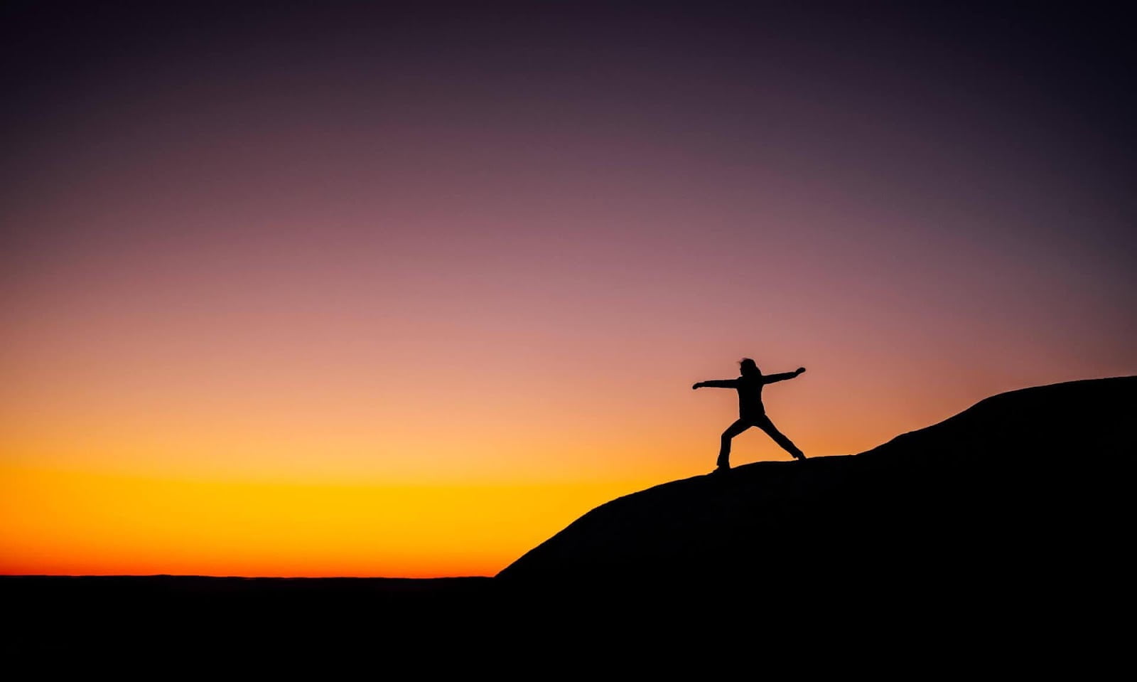 A person standing on a hill with a sunset in the backgroundDescription automatically generated with medium confidence